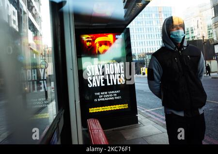 Un giovane uomo che indossa una maschera facciale attende accanto a messaggi governativi che dicono alle persone di rimanere a casa, esposto a una fermata dell'autobus a Whitechapel a Londra, Inghilterra, il 9 gennaio 2021. L'Inghilterra ha iniziato un terzo blocco nazionale martedì in un tentativo di arginare la trasmissione del coronavirus in tutto il paese. Nella capitale, il sindaco di Londra Sadiq Khan ha dichiarato ieri un 'incidente principale' per la città sulle pressioni di coronavirus, avvertendo che gli ospedali potrebbero presto essere sopraffatti con pazienti con covid-19. (Foto di David Cliff/NurPhoto) Foto Stock