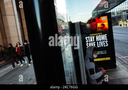 Un giovane uomo che indossa una maschera facciale attende accanto a messaggi governativi che dicono alle persone di rimanere a casa, esposto a una fermata dell'autobus a Whitechapel a Londra, Inghilterra, il 9 gennaio 2021. L'Inghilterra ha iniziato un terzo blocco nazionale martedì in un tentativo di arginare la trasmissione del coronavirus in tutto il paese. Nella capitale, il sindaco di Londra Sadiq Khan ha dichiarato ieri un 'incidente principale' per la città sulle pressioni di coronavirus, avvertendo che gli ospedali potrebbero presto essere sopraffatti con pazienti con covid-19. (Foto di David Cliff/NurPhoto) Foto Stock