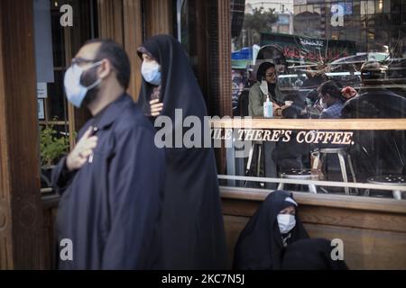 Un uomo iraniano e due donne velate che indossano maschere protettive si battono mentre assistono a una cerimonia religiosa per commemorare l'anniversario della morte di Fatima, figlia del Profeta Mohammad, nel centro di Teheran, mentre una donna siede in un bar in mezzo alla nuova epidemia di coronavirus (COVID-19) in Iran, Il 17 gennaio 2021. L'organizzazione mondiale della sanità ha annunciato il secondo anno dell'epidemia COVID-19 può essere peggiore del suo primo anno, dopo questa consapevolezza, i funzionari sanitari iraniani hanno chiesto alle persone di aiutare il paese a superare questo difficile periodo mantenendo l'allontanamento sociale e i protocolli sanitari. (Foto di Mortez Foto Stock