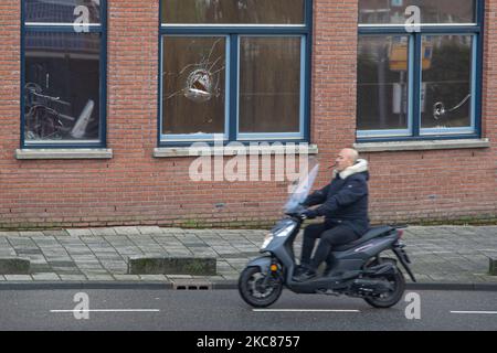 Una motocicletta passa davanti a un edificio con vetri rotti. Le conseguenze dei disordini anti-coprifuoco a Rotterdam. Finestre danneggiate di negozi, caffè, catena di fast-food, marciapiede distrutto, macchine ATM rotte, La fermata dell'autobus, le fermate del tram, le finestre e i vetri danneggiati anche in una zona residenziale sono stati causati dai violenti manifestanti che si sono scontrati con la polizia e saccheggiati la zona intorno a Groene Hilledijk, Beijerlandselaan e Randweg. È la 3rd notte consecutiva di rivolte e scontri con le politiche dopo che il governo ha imposto il coprifuoco per combattere la diffusione della pandemia di Coronavirus del Covid-19 Foto Stock