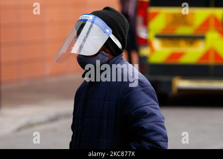 Un membro del pubblico che indossa una maschera facciale e uno scudo facciale passa davanti alle ambulanze al di fuori del dipartimento di emergenza del Royal London Hospital di Londra, Inghilterra, il 26 gennaio 2021. I dati degli organismi ufficiali di statistica del Regno Unito hanno rivelato oggi che, sulla base dei certificati di morte, fino al 15 gennaio di quest'anno quasi 104.000 persone sono morte con coronavirus dall'inizio della pandemia. Le cifre del governo, che si basano su decessi entro 28 giorni da un test positivo di covid-19, rimangono leggermente inferiori, ieri in piedi a 98.531. (Foto di David Cliff/NurPhoto) Foto Stock