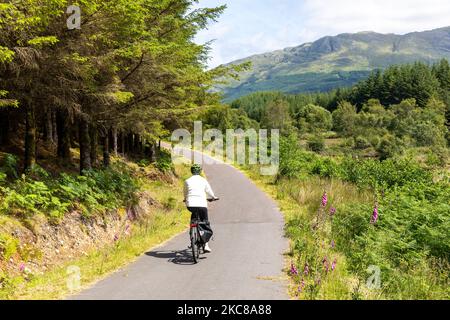 Modello rilasciato donna di mezza età cavalca bici elettrica in Scozia sulla strada ciclabile Caledonia strada vicino Oban, Scozia, Regno Unito, estate 2022 Foto Stock