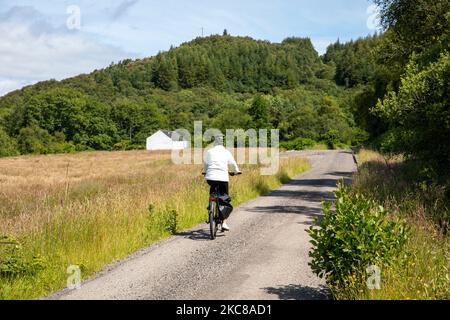 Modello rilasciato donna di mezza età cavalca bici elettrica in Scozia sulla strada ciclabile Caledonia strada vicino Oban, Scozia, Regno Unito, estate 2022 Foto Stock