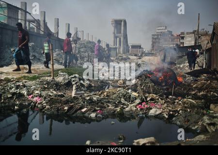 La gente si muove mentre il fuoco di immondizia genera il fumo tossico in un'area a basso reddito sul bordo esterno di Dhaka, Bangladesh lunedì 08 febbraio 2021. Secondo uno studio, l'inquinamento atmosferico riduce di 7 anni l'aspettativa di vita. (Foto di Syed Mahamudur Rahman/NurPhoto) Foto Stock