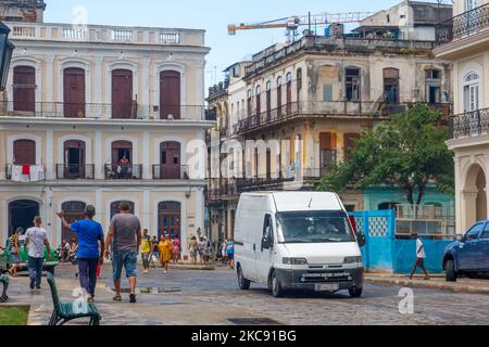 Un veicolo e il popolo cubano si trovano in una strada cittadina dove l'architettura alterata è comune Foto Stock