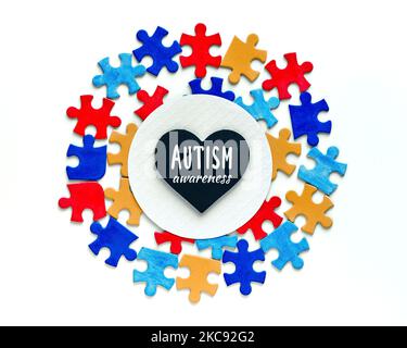 Testo di consapevolezza autismo su cuore nero, lavagna a forma di cuore, lavagna a gesso su cerchio di carta bianca incorniciata con pezzi di puzzle. Simbolo di consapevolezza dell'autismo Foto Stock