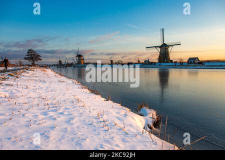 Una magica scriglia intorno al tramonto e crepuscolo con il cielo limpido d'inverno ai canali ghiacciati e ai mulini a vento di Kinderdijk nei Paesi Bassi. Il paese sta affrontando il clima artico, le temperature basse severe, le nevicate ed i venti alti dovuto la tempesta Darcy che ha causato i problemi nei trasporti e nella vita di tutti i giorni. Molti dei canali sono stati ghiacciati perché la temperatura è inferiore a zero a causa del clima freddo che a volte raggiunge i -16C, mentre il terreno è coperto di neve. Kinderdijk e i mulini a vento nel polder Alblasserwaard, è una famosa attrazione, un punto di riferimento olandese e un sito patrimonio dell'umanità dell'UNESCO, attrazione Foto Stock