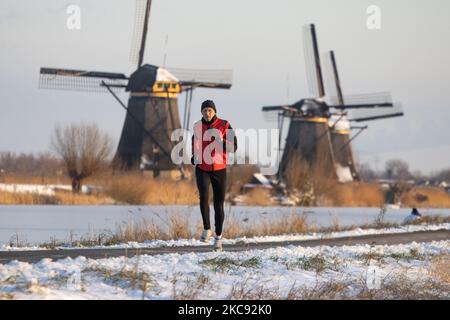 Un uomo con giacca rossa come visto correre nella neve a Kinderdijk. Una magica scriglia intorno al tramonto e crepuscolo con il cielo limpido d'inverno ai canali ghiacciati e ai mulini a vento di Kinderdijk nei Paesi Bassi. Il paese sta affrontando il clima artico, le temperature basse severe, le nevicate ed i venti alti dovuto la tempesta Darcy che ha causato i problemi nei trasporti e nella vita di tutti i giorni. Molti dei canali sono stati ghiacciati perché la temperatura è inferiore a zero a causa del clima freddo che a volte raggiunge i -16C, mentre il terreno è coperto di neve. Kinderdijk e i mulini a vento nel polder Alblasserwaard, è un'attrazione famosa Foto Stock