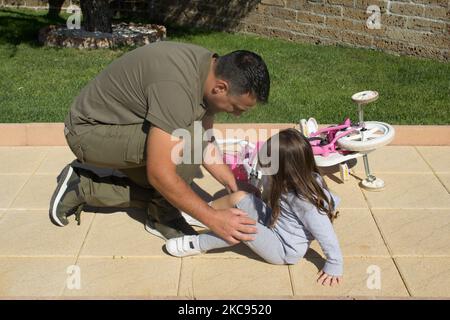 Immagine di un giovane papà che aiuta sua figlia che è caduta sulla sua bicicletta e ha un ginocchio scuoiata. Bambina alla ricerca di aiuto dopo la caduta con la sua bicicletta Foto Stock