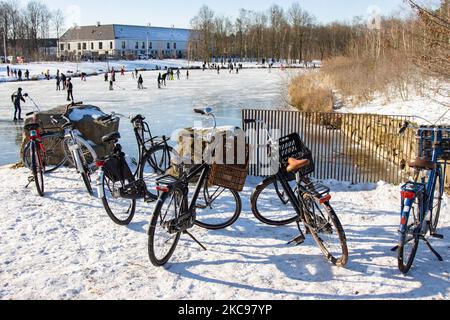 Biciclette parcheggiate accanto a un lago ghiacciato mentre la gente sta pattinando sul ghiaccio. La gente nei Paesi Bassi gode di un clima nevoso freddo di una settimana, con temperature inferiori allo zero, che si traduce in laghi, stagni e canali da congelare. Nel Parco Meerland vicino alla città di Eindhoven, durante una giornata di sole con il cielo blu, si possono ammirare folle di turisti per divertirsi pattinando sul ghiaccio, una tradizione olandese, camminando sul ghiaccio dei laghi ghiacciati, giocando con le loro slitte, pedalando o giocando a hockey su ghiaccio. Parco Meerland, Paesi Bassi il 13 febbraio 2021 (Foto di Nicolas Economou/NurPhoto) Foto Stock