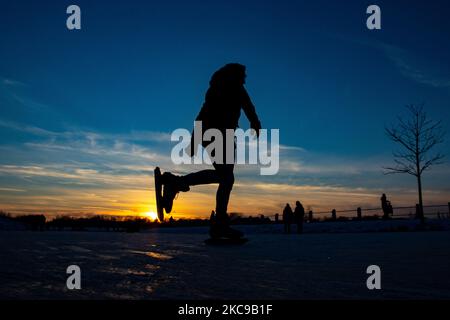 Silhouette scure di persone mentre pattina sul ghiaccio cristallino lago naturale ghiacciato nella regione del Brabante Nord nel pomeriggio prima del tramonto. La frenesia del pattinaggio su ghiaccio prende il controllo dei Paesi Bassi. Gli olandesi si divertono e si godono il freddo clima di una settimana con temperature inferiori allo zero, con laghi, insenature, stagni, fiumi e canali da congelare. Le folle sono state iceskating nel Parco Meerland vicino alla città di Eindhoven, durante una giornata di sole cielo blu, come è una tradizione olandese, le persone sono anche viste all'aperto nella natura ghiacciata e l'ambiente freddo camminando sul ghiaccio dei laghi ghiacciati, p Foto Stock