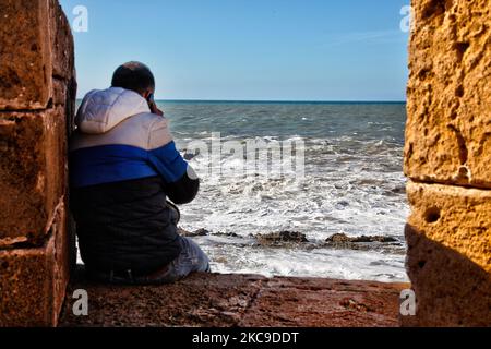 Uomo seduto in cima alle vecchie mura fortificate nella città costiera di Essaouira, Marocco, Africa. Essaouira è una città portuale e resort sulla costa atlantica del Marocco. La sua medina (città vecchia) è protetta da bastioni lungomare del 18th ° secolo chiamati Skala de la Kasbah, che sono stati progettati da ingegneri europei. Vecchi cannoni di ottone fiancano le pareti e ci sono vedute dell'oceano. (Foto di Creative Touch Imaging Ltd./NurPhoto) Foto Stock