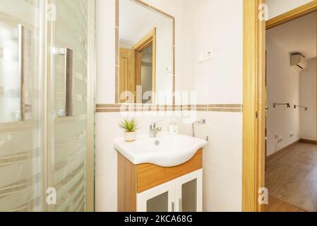 Bagno con cabina doccia, specchio incassato nella parete, bordi in porcellana e lavabo su mobile in legno Foto Stock