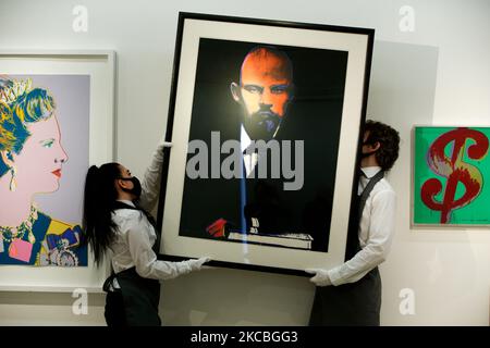 I gestori d'arte si pongono tenendo 'Lenin' (R), dell'artista americano Andy Warhol, stimato a GBP50.000-70.000, e tra uno dei quattro set di Warhol 'Regina Margarethe II di Danimarca, da: Regning Queens (Royal Edition)' (L), stimato a GBP60.000-80.000, e '($)1' (R) di Warhol, stimato a GBP40.000-60.000, durante un'anteprima alla casa d'aste di Christie a Londra, Inghilterra, il 26 marzo 2021. (Foto di David Cliff/NurPhoto) Foto Stock