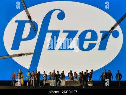 Siringhe mediche e piccole figurine di persone sono visti di fronte al logo Pfizer visualizzato su uno schermo. Sabato 26 marzo 2021 a Dublino, Irlanda. (Foto di Artur Widak/NurPhoto) Foto Stock