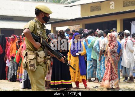 Il personale addetto alla sicurezza è in guardia mentre gli elettori si accodano per esprimere i loro voti durante la prima fase delle elezioni dell'Assemblea di Assam, in un seggio elettorale nella circoscrizione di Batadrawa, nel distretto di Nagaon, ad Assam, sabato 27 marzo 2021. (Foto di David Talukdar/NurPhoto) Foto Stock