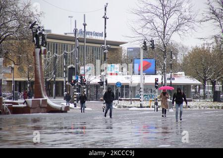 La gente è vista camminare con la stazione ferroviaria centrale di Eindhoven sullo sfondo. Il terzo giorno dell'insolita nevicata di aprile nei Paesi Bassi, il paese si risveglia sulla neve coperta dopo un'intensa nevicata mattutina, un evento bizzarro per aprile. Il 3rd° giorno di basse temperature e nevicate nei Paesi Bassi dopo il lunedì di 'Pasqua Bianca' con un significativo calo di temperatura, raggiungendo il punto di congelamento secondo l'agenzia meteorologica olandese KNMI rendendo il lunedì di Pasqua uno dei giorni più freddi mai registrati con basse temperature. Oltre alla neve, grandine e vento forte ghiaccio-freddo ad alta velocità occurr Foto Stock