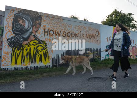 Una donna cammina il suo cane di fronte a un nuovo murale di CHELS (Chelsea Jacobs, un'artista americana che vive a Dublino), situato nella zona del Grand Canal Docs, che rappresenta un bambino in una maschera a gas, con una scritta che legge 'How Soon is Now?'. Domenica 18 aprile 2021 a Dublino, Irlanda. (Foto di Artur Widak/NurPhoto) Foto Stock