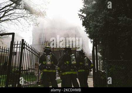 I vigili del fuoco osservano che la casa emette fumo dal fuoco della storica casa di Palmer Square, Chicago, USA, il 27 aprile 2021. Un incendio scoppiò a 2228 N. Kedzie Avenue in Palmer Square a circa 3:45pm CST. L'incendio è stato presumibilmente causato da lavori in soffitta e sul tetto. Un operaio soluto ha combattuto il fuoco fino a quando il Dipartimento dei vigili del fuoco di Chicago non è arrivato sulla scena. Una casa anziana adiacente è stata evacuata per motivi di sicurezza. La donna che vive nella residenza è scappata intatta, e un vigile del fuoco è stato portato via da EMS con lesioni non pericolose per la vita. (Foto di Jim Vondruska/NurPhoto) Foto Stock