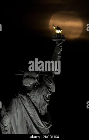Il Super Flower Moon sorge dietro la Statua della libertà a New York City, Stati Uniti il 27 aprile 2021, come visto da Jersey City, New Jersey. (Foto di Deccio Serrano/NurPhoto) Foto Stock