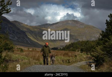 Padre Krzysztof Sikora cammina il suo cane 'Rambo' vicino alla cittadina di Barnanoraun, vicino al fiume Owenglin. Geograficamente, la parrocchia di Roundstone è considerata la più grande parrocchia d'Irlanda e si estende dalle spiagge di Gurteen ai Monti Twelve Bens e Mám Tuirc. Fino agli anni '1990s la parrocchia era servita da tre sacerdoti, ora CE n'è una sola che si occupa di cinque chiese. L'attuale Parroco, padre Krzysztof Sikora, nato in Polonia, è membro della congregazione religiosa dei Missionari del Verbo Divino. Dopo anni di lavoro missionario nelle Filippine, in Germania e in Polonia, si stabilì in Irlanda Foto Stock