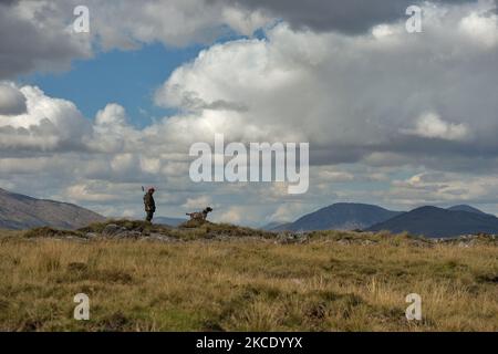 Padre Krzysztof Sikora visto con il suo cane 'Rambo' vicino alla pesca di Gowla, situato nel centro di Connemara, tra uno dei paesaggi più belli e tranquilli. Geograficamente, la parrocchia di Roundstone è considerata la più grande parrocchia d'Irlanda e si estende dalle spiagge di Gurteen ai Monti Twelve Bens e Mám Tuirc. Fino agli anni '1990s la parrocchia era servita da tre sacerdoti, ora CE n'è una sola che si occupa di cinque chiese. L'attuale Parroco, padre Krzysztof Sikora, nato in Polonia, è membro della congregazione religiosa dei Missionari del Verbo Divino. Dopo anni di lavoro come missio Foto Stock