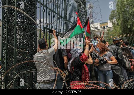 I manifestanti alzano le bandiere palestinesi e sollevano pugni davanti alla porta del Parlamento tunisino dopo aver rimosso il filo spinato, durante una manifestazione svoltasi di fronte all'edificio del parlamento tunisino nella città di Bardo Tunisi, in Tunisia, il 18 maggio 2021; Chiedere l'adozione da parte del parlamento di una legge che criminalizzi tutte le forme di normalizzazione delle relazioni con Israele. I dimostranti hanno protestato anche contro gli attacchi aerei israeliani sulla striscia di Gaza e contro le violazioni israeliane nei territori occupati in Palestina, in particolare nel quartiere palestinese Sheikh Jarrah, a Jerus orientale Foto Stock