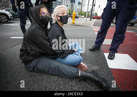 Weronika (20, L) e Lu (21, R) bloccano un furgone a Varsavia, Polonia il 19 maggio 2021. Gli attivisti anti-aborto in un furgone che mostra immagini grafiche di feti abortiti sono stati fermati da attivisti pro-scelta nel centro di Varsavia, Polonia. L'attivista Weronika, ventenne, si è seduto sulla strada di fronte all'autobus, in quanto si trovava all'uscita della trafficata rotonda ONZ. Gli autisti dell’autobus suonavano un forte allarme attraverso gli altoparlanti del furgone nel tentativo di scongiurare l’attivista. Altre due donne, Magda e Lu, si accovacciarono sotto l'autobus. Diverse dozzine di poliziotti arrivarono presto sulla scena e gli attivisti furono dati f Foto Stock