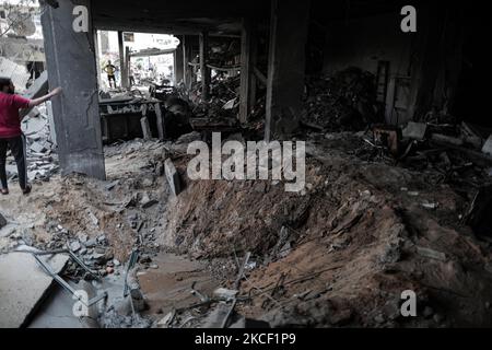 Le persone ispezionano un buco e le macerie di un edificio residenziale distrutto che è stato colpito da attacchi aerei israeliani, a Gaza City, giovedì 20 maggio 2021.(Photo by Momen Faiz/NurPhoto) Foto Stock