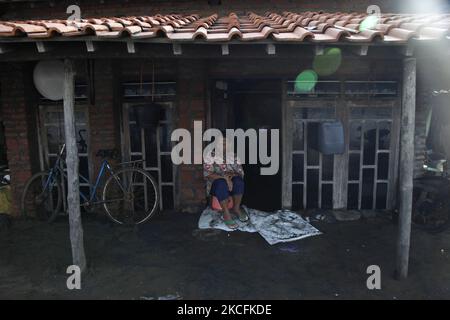 Una donna seduta di fronte alla sua casa che in parte sepolta dalla sabbia a causa delle onde maree nel villaggio di Simonet, costa settentrionale della città di Pekalonga, provincia di Giava Centrale, il 4 giugno 2021. Sulla base dei dati dell'Agenzia geologica del Ministero indonesiano dell'energia e delle risorse minerarie, la città di Pekalonga sta vivendo una subsidenza di terra di 6 centimetri all'anno, causata dal cambiamento climatico globale, e l'uso massiccio delle acque sotterranee da housholds, agricoltura, industria, che, se non immediatamente mitigato, la città è prevista affondare nel 2036. (Foto di Aditya Irawan/NurPhoto) Foto Stock