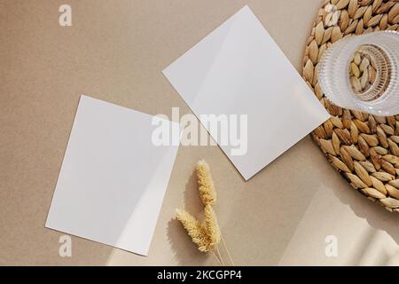 Due carte bianche bianche bianche su sfondo beige, con erba secca, vista dall'alto. Moderno minimal mock-up Foto Stock