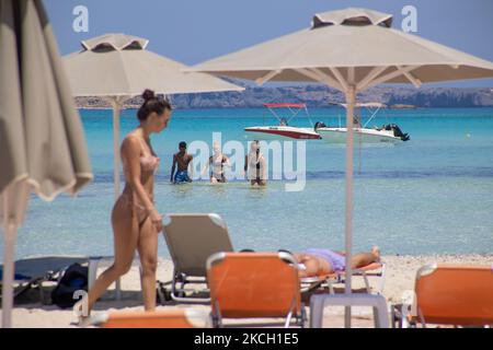 Giovani nel mare di Balos attraverso il Beach Bar con costume da bagno e bikini. Vista panoramica della spiaggia di Balos, l'incredibile laguna con le acque turchesi esotiche e tropicali del Mar Mediterraneo si trova nella regione di Chania, sull'isola di Creta. Balos è una delle spiagge più visitate di Creta e popolare per i visitatori di tutto il mondo. Acque cristalline, la laguna, montagne rocciose ripide, un bar sulla spiaggia che fornisce ombrelloni e ombra con bevande e un'isola pirata si trovano nella stessa regione che è accessibile da un trekking di 20 minuti o in barca. La Grecia sta cercando di rilanciare il suo turismo e la sua giv Foto Stock