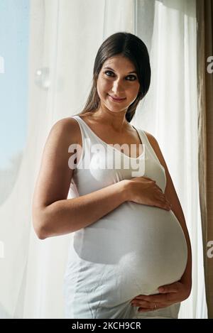 Im innamorato di una persona che non ho ancora incontrato. Ritratto di una donna incinta che cullava il ventre mentre si era in piedi davanti a una finestra a casa. Foto Stock