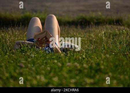 Una donna sta leggendo un libro sdraiata sull'erba vicino al Castello reale di Wawel e al fiume Vistola di Cracovia. Sabato 24 luglio 2021, a Cracovia, Malopolskie Voivodato, Polonia. (Foto di Artur Widak/NurPhoto) Foto Stock