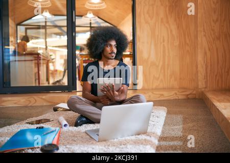 Lavorare attraverso modi per trarre profitto dalla sua passione. Un giovane designer che lavora sul pavimento in un ufficio. Foto Stock