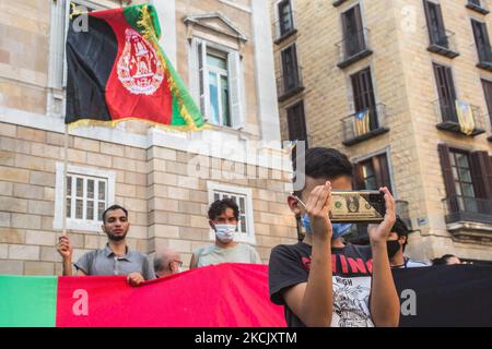 Il ragazzo che guarda un cellulare con un caso da un dollaro è visto davanti ai manifestanti con una bandiera afghana. Circa cinquecento persone hanno manifestato a Barcellona in solidarietà con le ragazze e le donne dell'Afghanistan e in difesa dei loro diritti sotto lo slogan "Afghanistan: Per una vita dignitosa e libera" (Photo by DAX Images/NurPhoto) Foto Stock