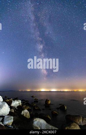 La Via Lattea nel buio cielo notturno greco con le stelle illuminanti, parte della galassia che contiene il nostro sistema solare visto da una spiaggia di sabbia in Halkidiki, Grecia con una barca visibile e villaggi dell'altro lato che riflettono la luce sulla superficie dell'acqua. La fotografia a lunga esposizione della Milkyway è stata catturata dalla spiaggia di sabbia di Koviou, un tipico paesaggio mediterraneo del Mar Egeo, vicino a Nikiti. A causa della pandemia di Coronavirus del Covid-19, la Grecia non era sovraffollata di turisti e di sicurezza - misure di blocco applicate durante l'estate, un fatto che ha aiutato il cielo a essere più scuro e t Foto Stock