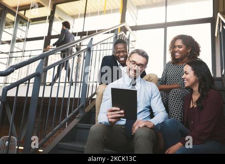 Pensare fuori dalla scatola significa pensare fuori dall'ufficio. Un gruppo di colleghi diversi ha un incontro improvvisato con un tablet sulle scale. Foto Stock