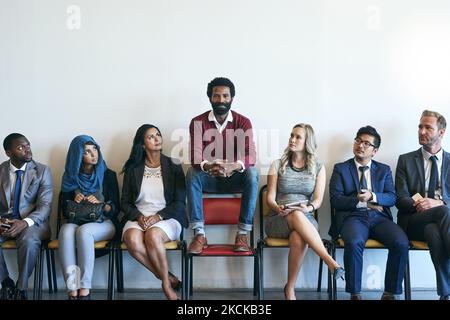 Distinguersi dalla folla. Ritratto di un candidato felice di lavoro seduto in fila con un gruppo di uomini d'affari ben vestiti. Foto Stock