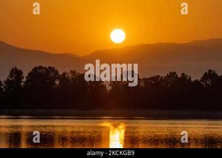 Ora magica alba estiva con colori caldi del cielo e il sole su Kerkini con uccelli, cavalli, pescatori locali di pesca macchiati come silhouette, al Parco Nazionale del Lago nella regione di Serres nel nord della Grecia. Il lago artificiale Kerkini è una zona umida unica, un Parco Nazionale e protetta dalla Convenzione di Ramsar come zona umida con migliaia di uccelli, tra cui la foresta rara e protetta lungo il fiume, in quanto si stanno sviluppando importanti idrobiosfere di grande importanza e accettazione a livello internazionale, La principale fonte d'acqua proveniente dal fiume Strymon proviene dalla Bulgaria. Lago Kerkini, Serres, Grecia il 30 agosto, Foto Stock