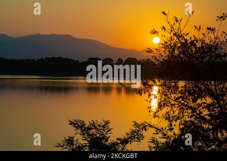 Ora magica alba estiva con colori caldi del cielo e il sole su Kerkini con uccelli, cavalli, pescatori locali di pesca macchiati come silhouette, al Parco Nazionale del Lago nella regione di Serres nel nord della Grecia. Il lago artificiale Kerkini è una zona umida unica, un Parco Nazionale e protetta dalla Convenzione di Ramsar come zona umida con migliaia di uccelli, tra cui la foresta rara e protetta lungo il fiume, in quanto si stanno sviluppando importanti idrobiosfere di grande importanza e accettazione a livello internazionale, La principale fonte d'acqua proveniente dal fiume Strymon proviene dalla Bulgaria. Lago Kerkini, Serres, Grecia il 30 agosto, Foto Stock