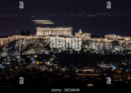 Vista notturna del Partenone e dell'Acropoli con un traghetto che passa sullo sfondo della capitale greca Athina. La tecnica fotografica a lunga esposizione mostra le antichità illuminate al buio con il paesaggio urbano della città intorno. L'antica collina dell'Acropoli, tra cui il tempio in marmo del Partenone, conosciuto in tutto il mondo, e i resti di molti edifici antichi di grande importanza architettonica e storica come l'Erechtheion, Propylaia, il tempio di Atena Nike, i cariadi e molto altro ancora. Durante l'occupazione ottomana, l'Acropoli fu reciso da gravi danni. Oggi è patrimonio mondiale dell'UNESCO Foto Stock