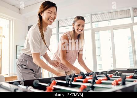 Football, donne e amici che giocano a calcio da tavolo in un ufficio per divertimento, legame e competizione sul lavoro con felicità, energia e motivazione Foto Stock