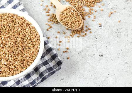 Grano saraceno in una ciotola bianca con cucchiaio di legno, grano saraceno crudo verde Foto Stock