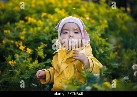 Foto di una ragazza felice con giacca gialla e cappello bianco che gioca in un prato, fiori circondati da un bambino e erba, che gioca nel campo d Foto Stock
