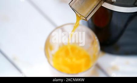 in primo piano, dalla centrifuga scorre il succo d'arancia appena spremuto in un bicchiere. vista dall'alto. Foto di alta qualità Foto Stock