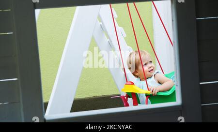 estate, in giardino, bella bambina di un anno che oscilla su un altalena nel parco giochi. Foto di alta qualità Foto Stock