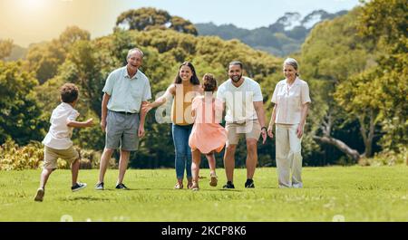 Grande famiglia, parco naturale e felice di giocare con i bambini che corrono sull'erba con i nonni anziani, mamma e papà sorridono nel sole estivo. Madre divertente Foto Stock