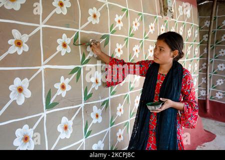 Una donna disegna motivi tradizionali su un muro della sua casa al villaggio di Tikoil a Nachole upazila del distretto di Chapainawabbanj del Bangladesh. (Foto di Mushfiqul Alam/NurPhoto) Foto Stock