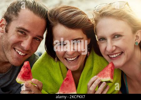 Amiamo una delizia dolce e succosa. Ritratto di un gruppo di giovani amici felici che mangiano cocomeri in spiaggia. Foto Stock